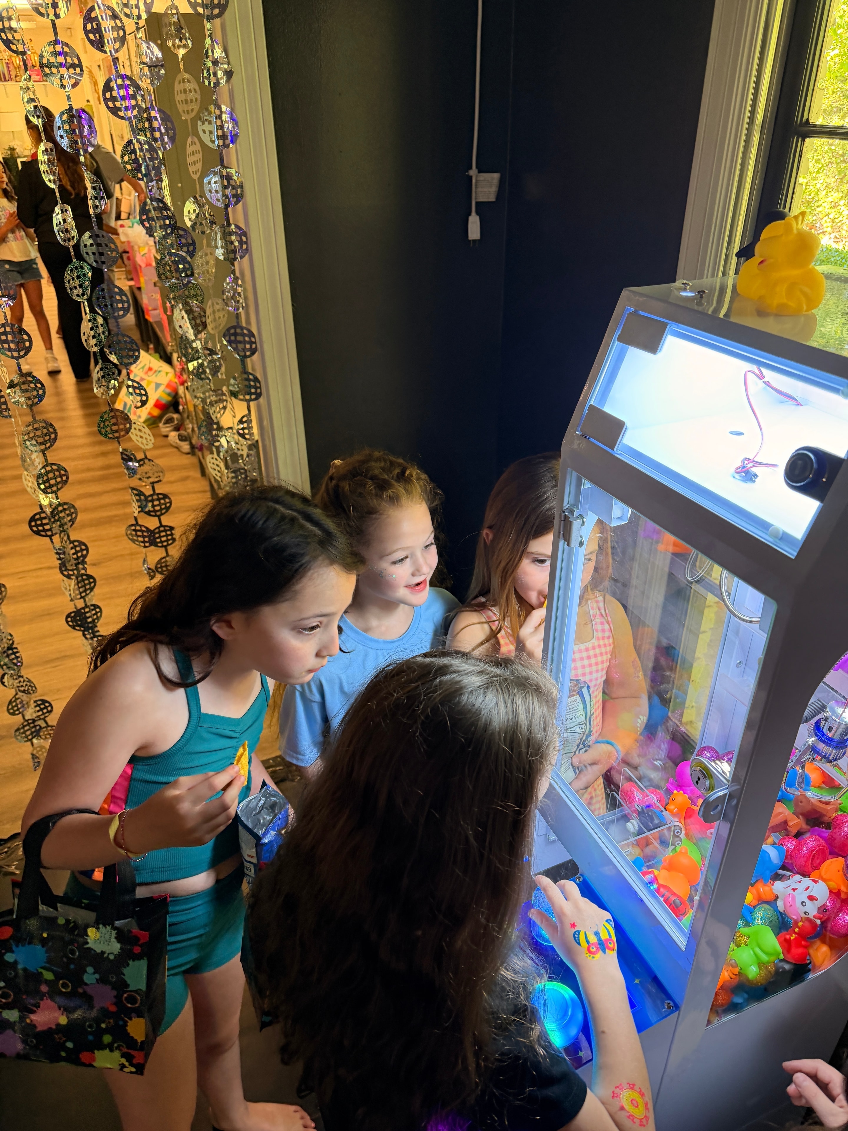 Girls gathered around mini crane machine at birthday party